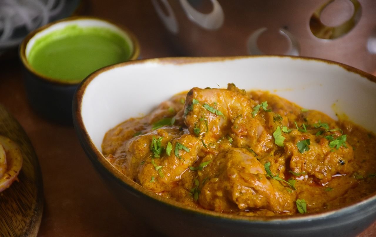 Delicious Indian chicken curry served in a bowl, garnished with fresh cilantro, alongside green chutney.